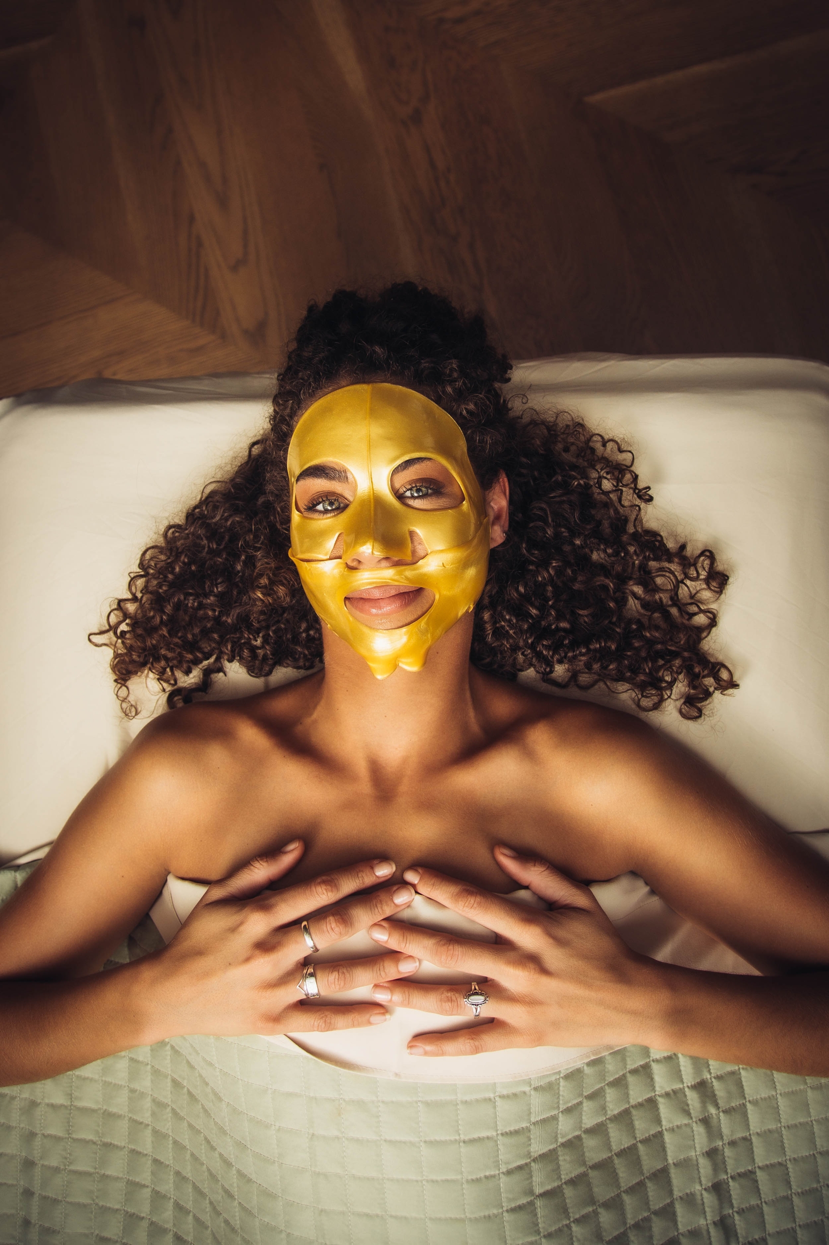 A woman at Neptune SPA, wearing a gold face mask is peacefully lying on a bed, indulging in a relaxing skincare routine.